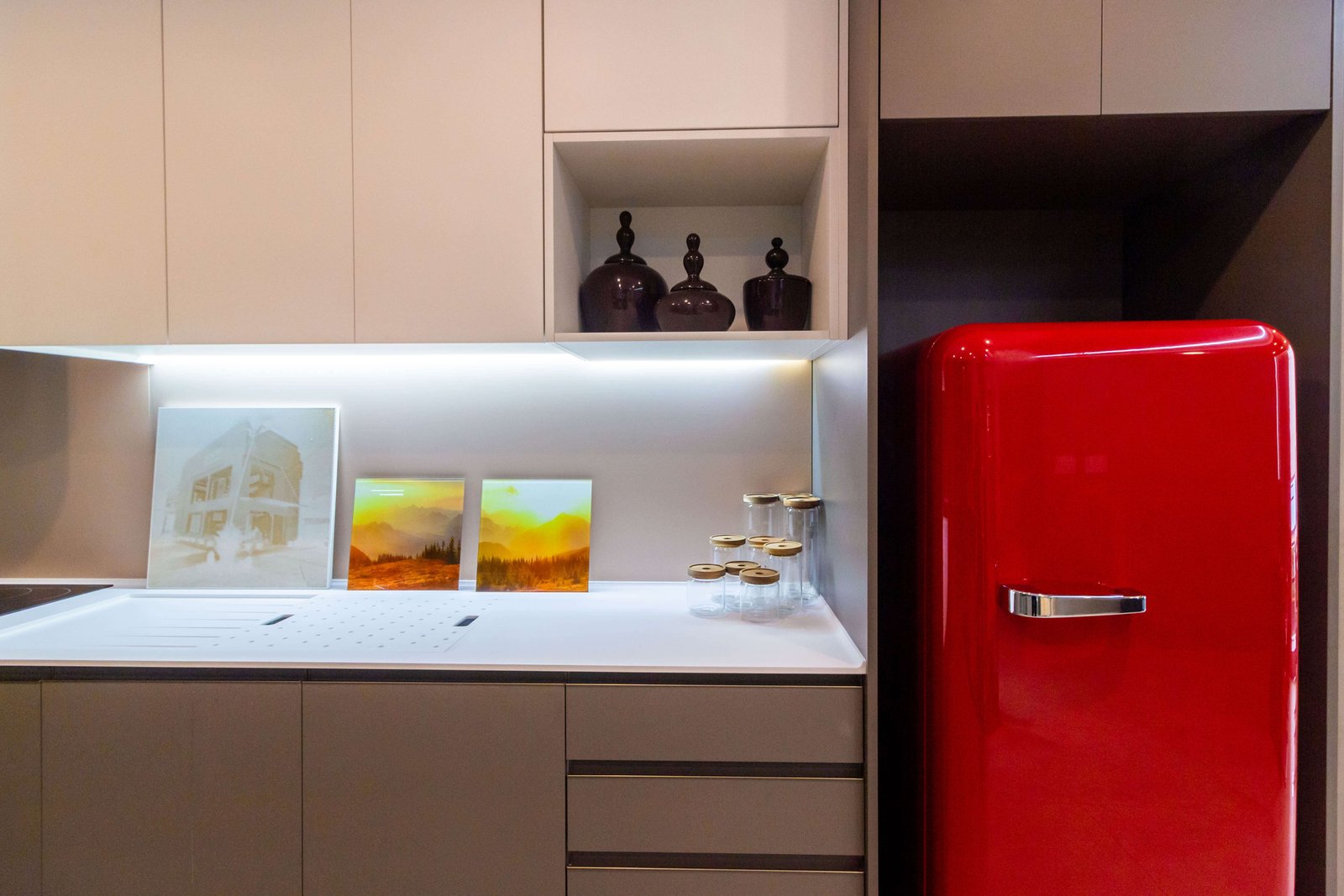 Detalhe da bancada da mesma cozinha, destacando uma geladeira vermelha estilo retrô vibrante ao lado da marcenaria planejada e iluminação de LED sob o armário superior.