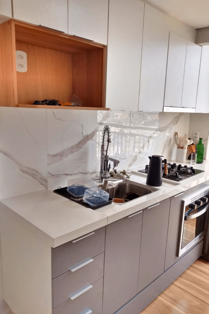 Close na área da pia da foto anterior, detalhando a continuidade do revestimento marmorizado na parede e a organização da bancada com escorredor e utensílios.