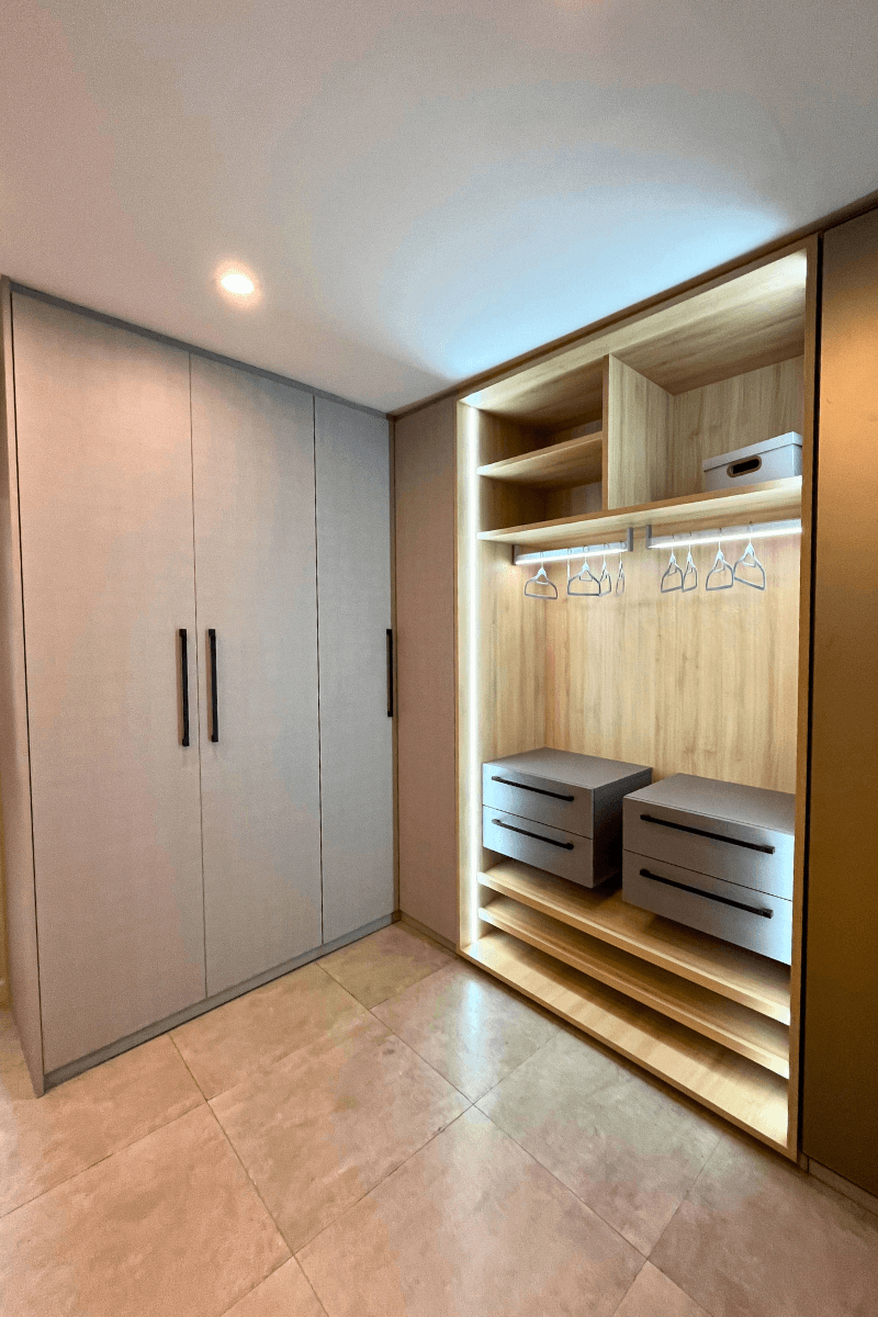 Um guarda-roupa sofisticado combinando portas fechadas em acabamento texturizado cinza claro e um nicho aberto com interior amadeirado, prateleiras e iluminação interna de destaque.