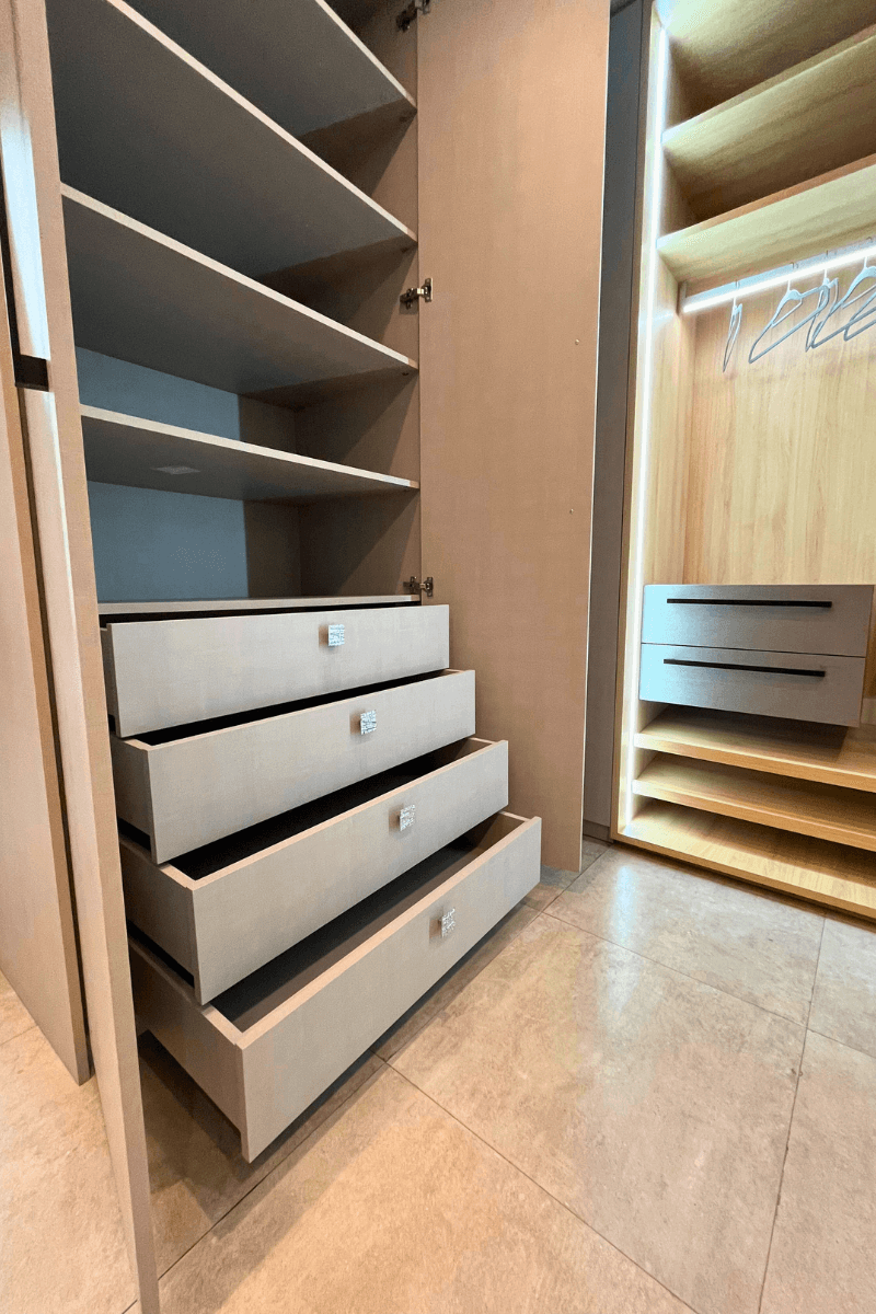 Vista interna de um armário aberto, focando em um gaveteiro com quatro gavetas de cor bege texturizada e puxadores modernos, além de prateleiras superiores.
