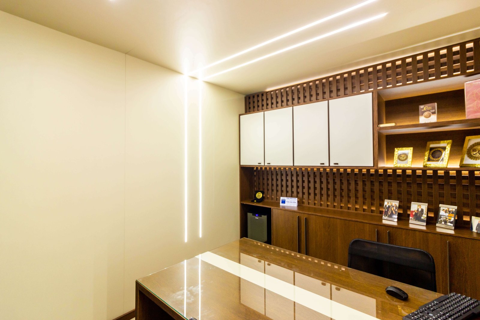 Visão ampla destacando o design de iluminação com fitas de LED contínuas que sobem pela parede e cruzam o teto, além da mesa de reuniões com tampo de vidro.